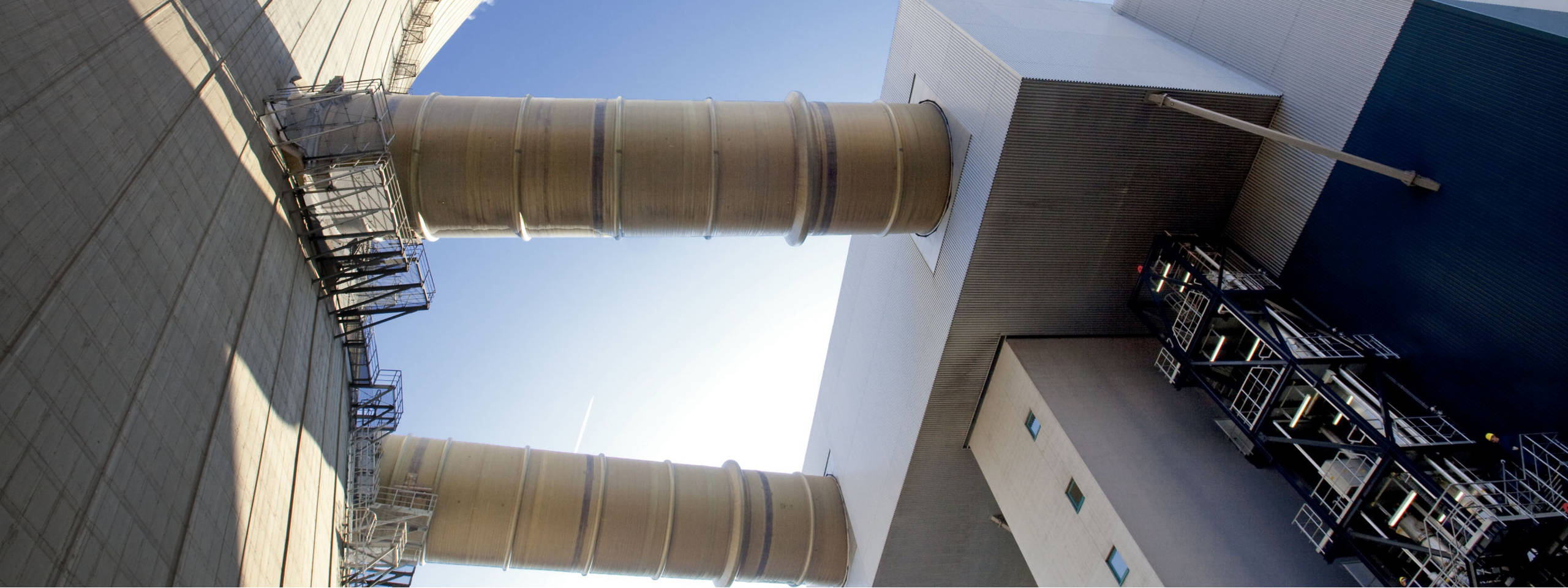 Industrieanlage mit zwei großen Rohren, einer Betonwand und einer modernen Gebäudestruktur im Hintergrund.