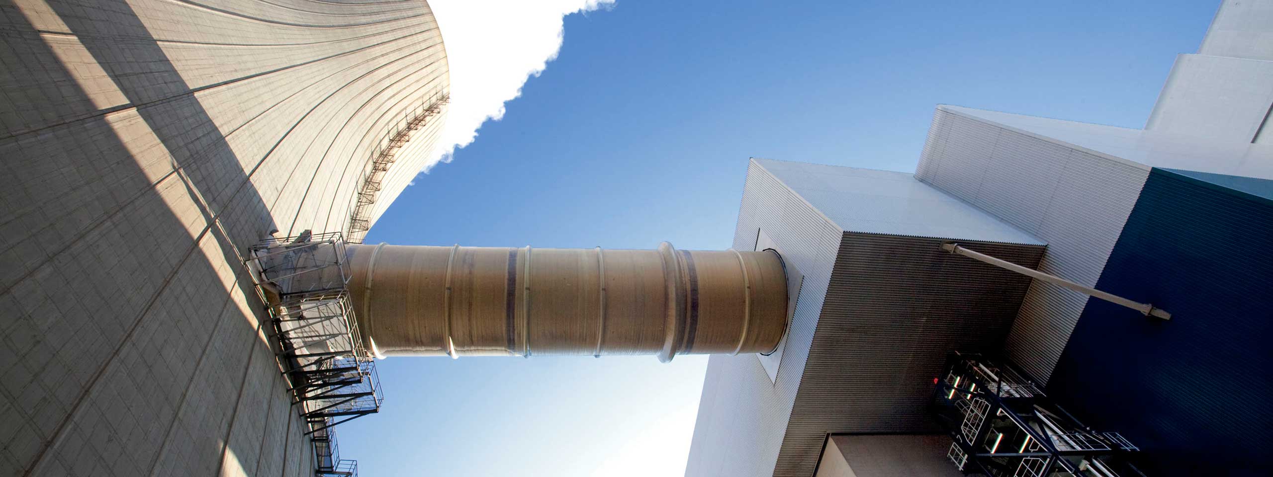 Ein Sichtfeld auf einen Kühlturm und ein Rohr unter blauem Himmel. Die Struktur zeigt industrielle Architektur.