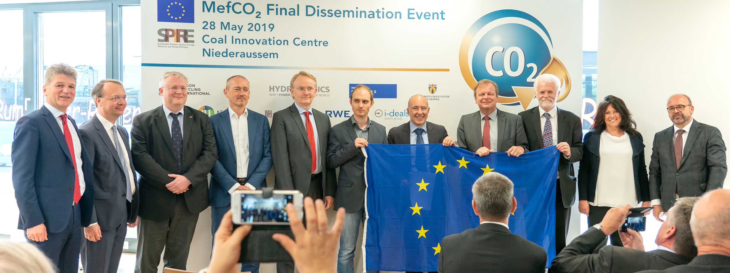 Die Gruppe posiert mit einer EU-Flagge während einer Veranstaltung im Coal Innovation Centre in Niederaußem.