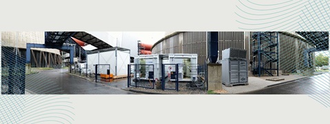 Eine industrielle Umgebung mit mehreren Containern, Zäunen und einem Außengelände neben großen Gebäuden.