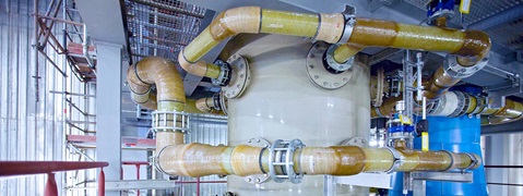 Ansicht von Rohren und einem großen Behälter in einer industriellen Umgebung mit Stahlgerüsten.