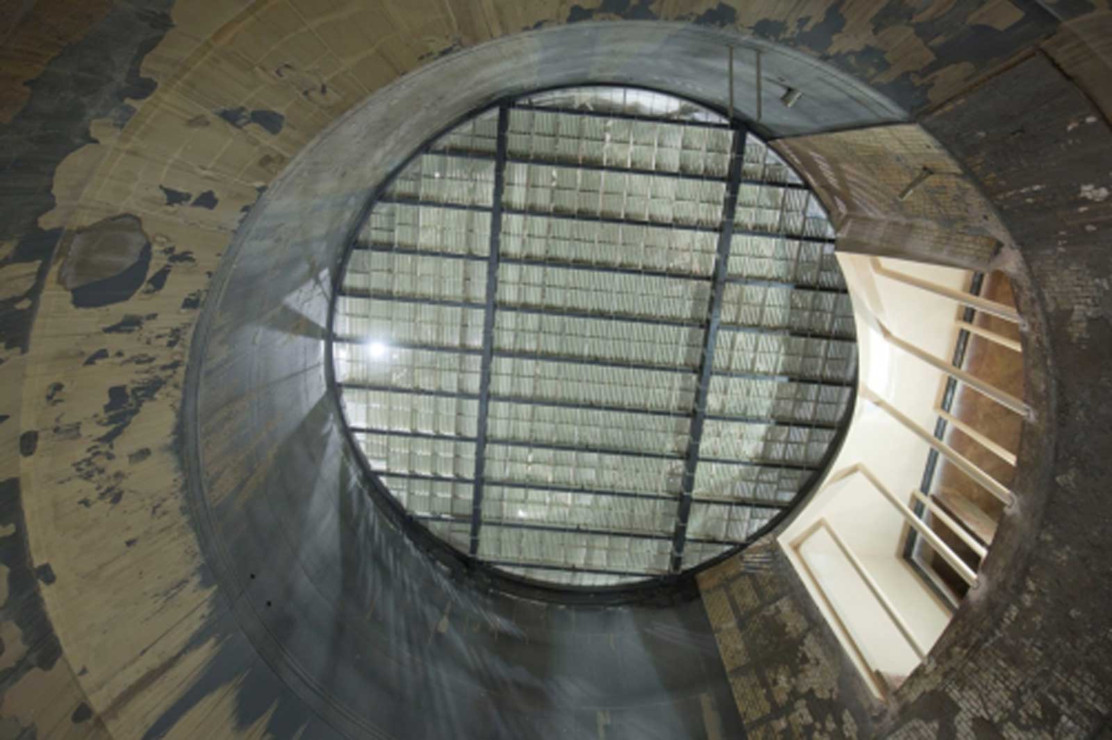 Blick nach oben in einen runden, alten Raum mit einer transparenten Decke und einem Treppenaufgang.
