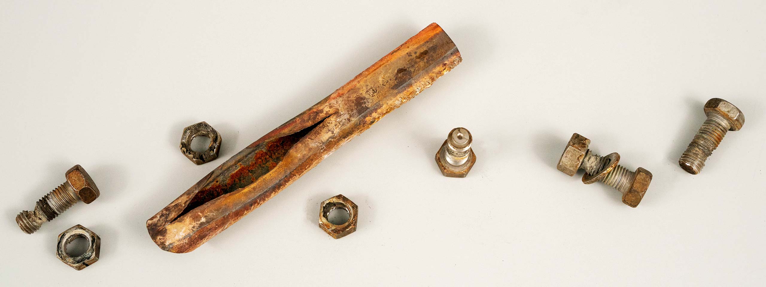 Ein rostiger Schraubenschlüssel, einige Schrauben und Unterlegscheiben auf einem hellen Hintergrund.
