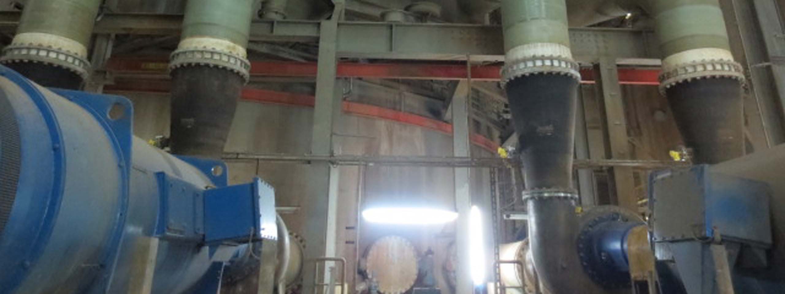 Ein Industrieinneres mit großen Rohren und Maschinen, die an einer Wand montiert sind, beleuchtet von einer Quelle im Hintergrund.