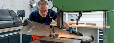 Ein Handwerker bearbeitet ein Stahlblech an einer Schneidemaschine in einer Werkstatt.