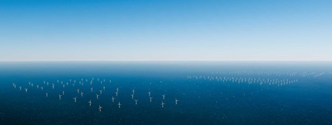 A wide view of offshore wind turbines in a calm blue sea, beneath a clear sky.