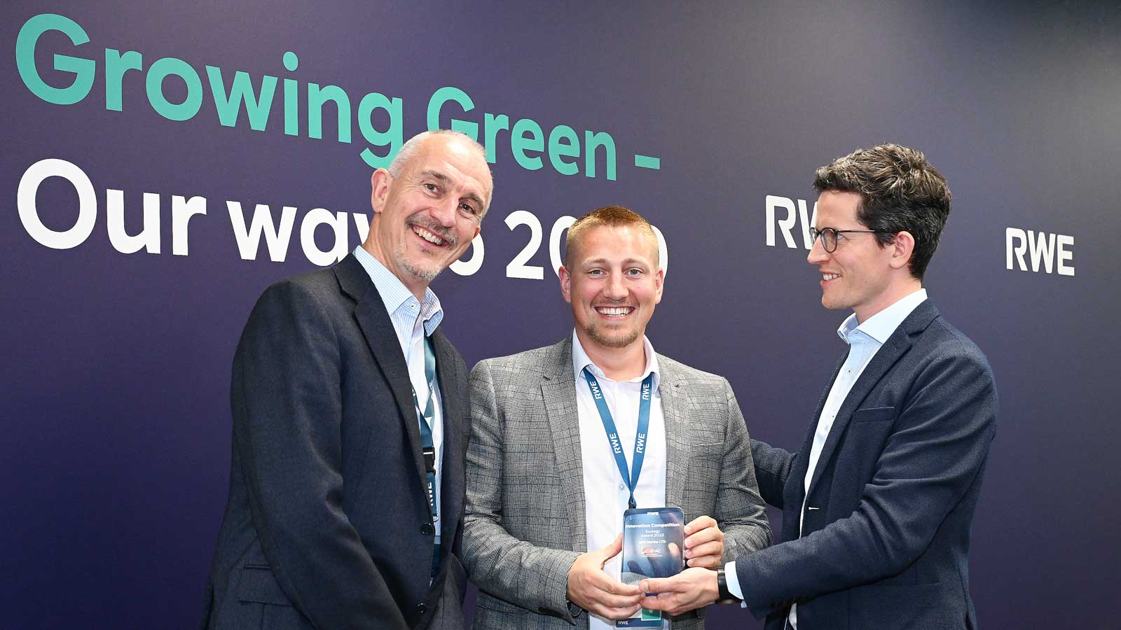 Three men pose together, holding a trophy against a dark blue backdrop with "Growing Green - Our way 2020" and "RWE" logos.