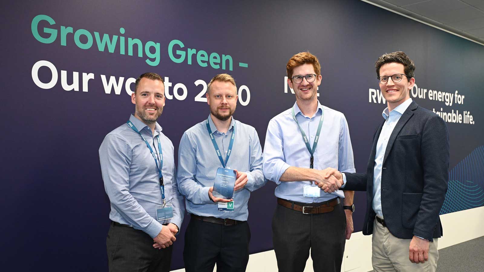 Vier Personen stehen vor einer Wand mit dem Text 'Growing Green - Our way to 2030' und schütteln Hände.