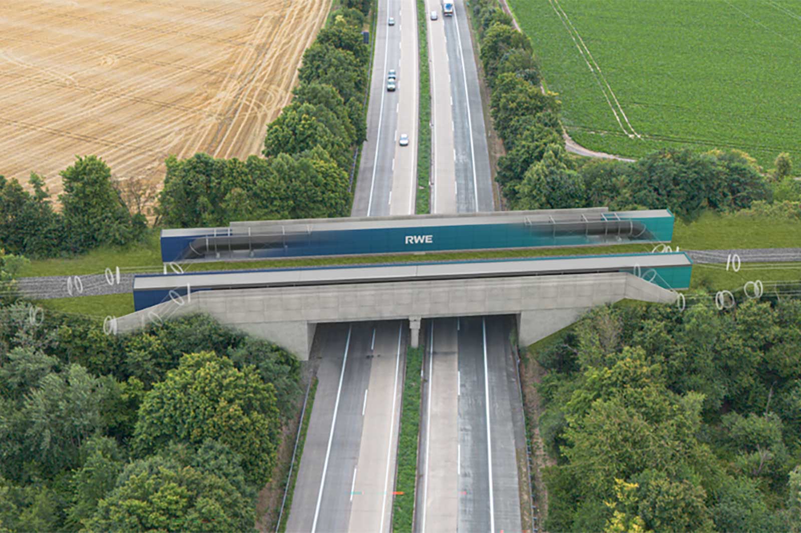 Luftaufnahme einer Autobahn unter einer Betonbruecke mit zwei langen gruenen RWE-Modulen, umgeben von Feldern, Baumen und Gleisen.