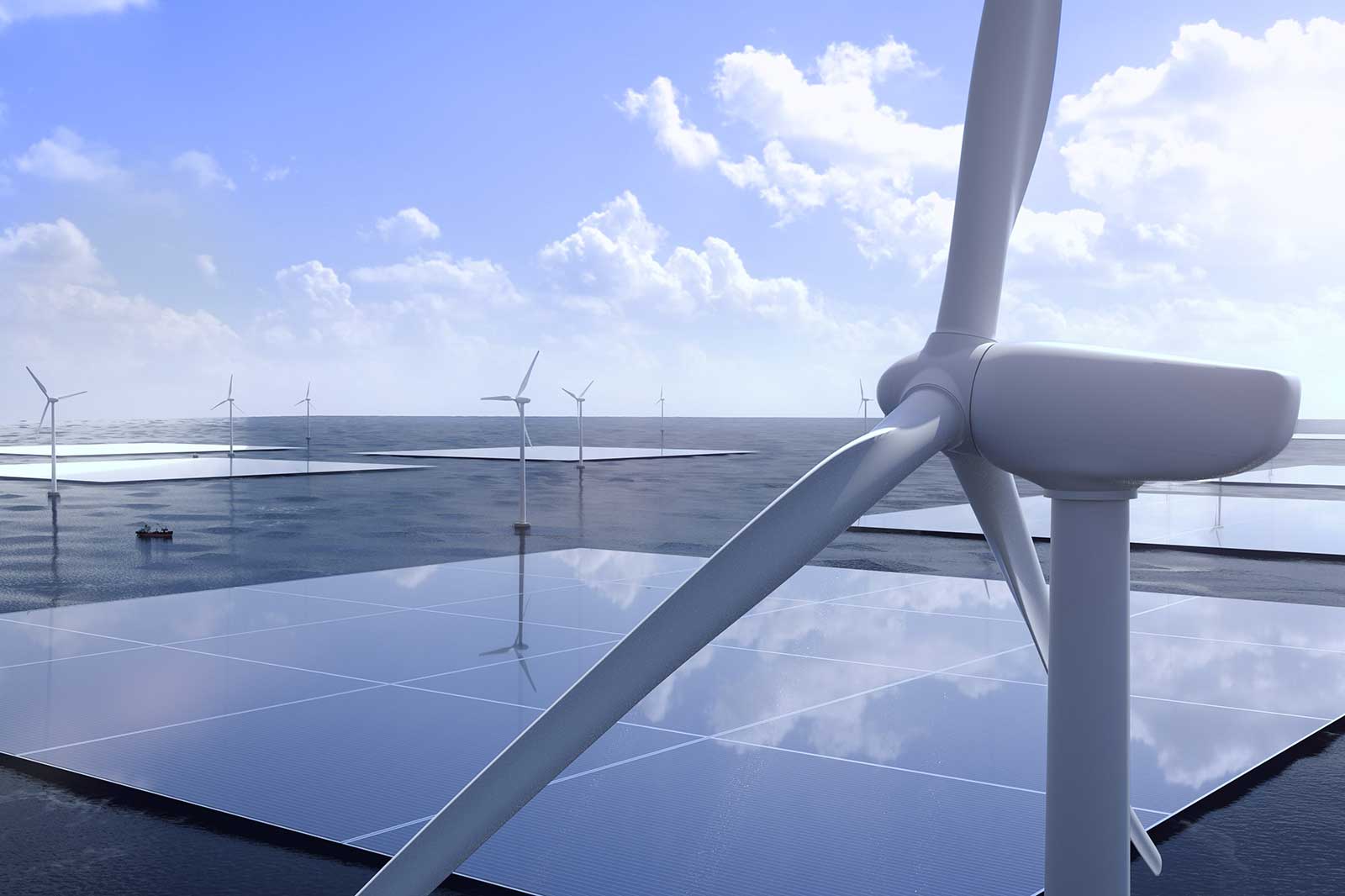 Wind turbines rotate above solar panels on calm water under a clear sky with clouds.