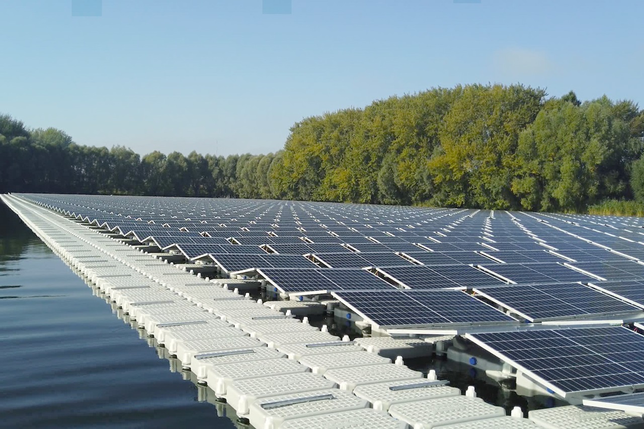 Schwimmende Solarpanels auf einem Gewässer, umgeben von Bäumen im Hintergrund, bei klarem Himmel.