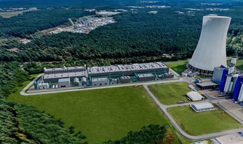 Eine Luftaufnahme eines Industriekomplexes mit großen Kühltürmen und grünen Gebäuden, umgeben von Wald.