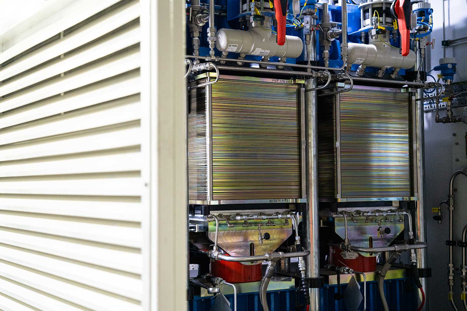 A view of two large metallic devices in a technical room, partially concealed by a white cabinet.