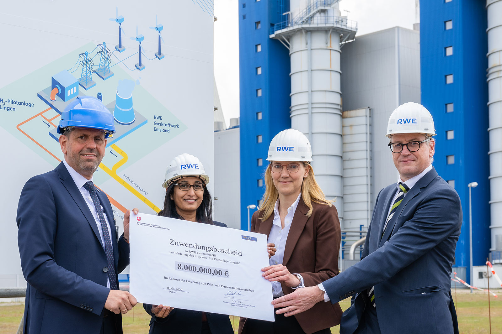 Vier Personen in Schutzhelmen präsentieren einen großen Scheck über 8.000.000 € vor einem Gas-Kraftwerk.