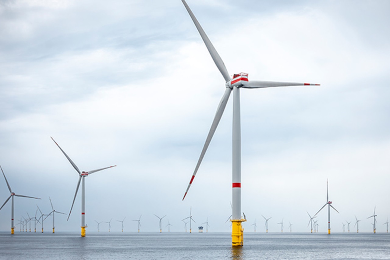 Offshore wind turbines stand in the water under a cloudy sky. Some turbines are turning in the wind.