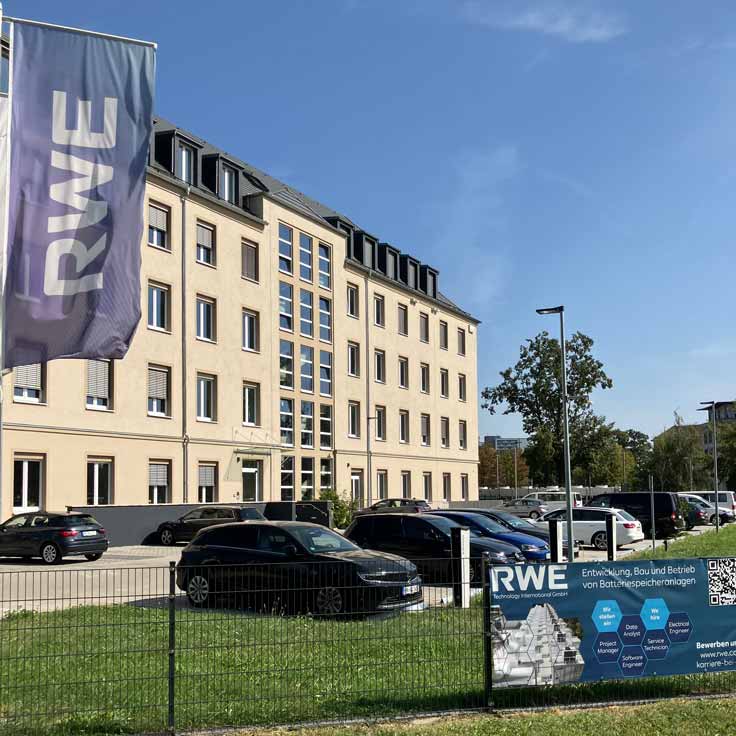A modern building displaying the RWE logo. Numerous cars are parked in front. An information banner is visible in the foreground.