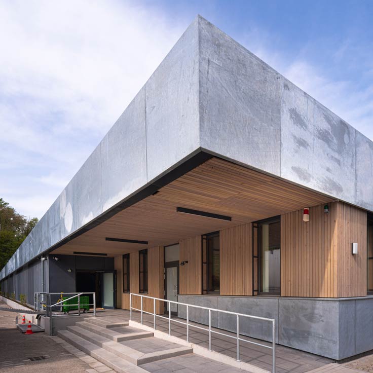 Ein modernes Gebäude mit einer Metall- und Holzfassade, großen Fenstern und Eingangstreppe.