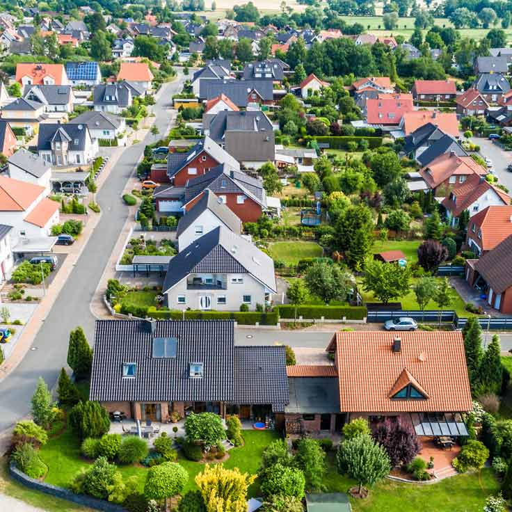 Vogelperspektive auf ein Wohngebiet mit verschiedenen Häusern, Gärten und von Bäumen gesäumten Straßen.