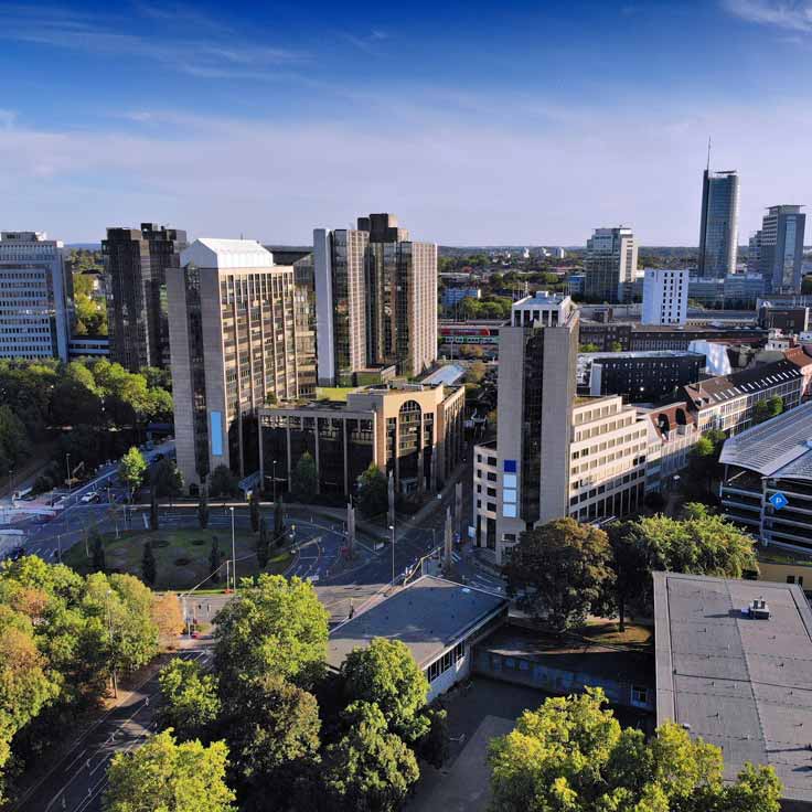 An aerial view of a modern city with tall buildings and abundant greenery in the surroundings.