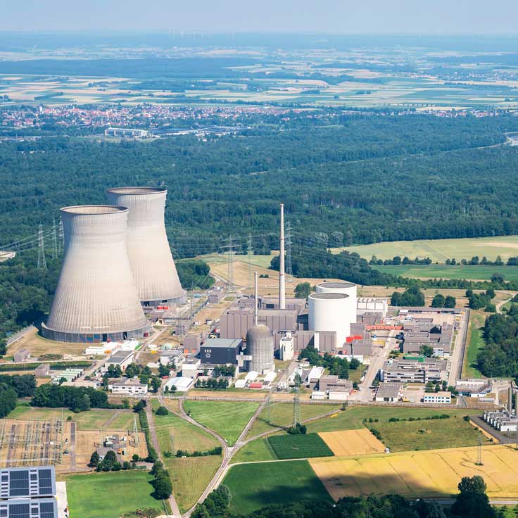 Eine Luftaufnahme eines Kernkraftwerks mit Kühltürmen, umgeben von grünen Feldern und Wäldern.