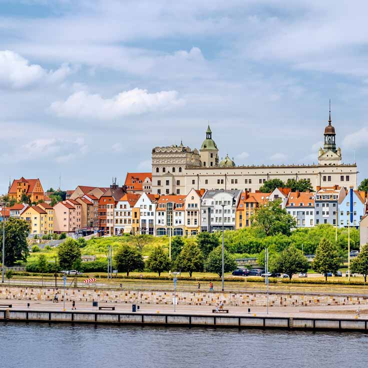 A picturesque view of colourful houses with a historic castle in the background, surrounded by trees and water.