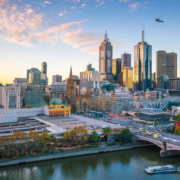 A panoramic view of Melbourne, featuring modern skyscrapers and the Yarra River in the foreground.