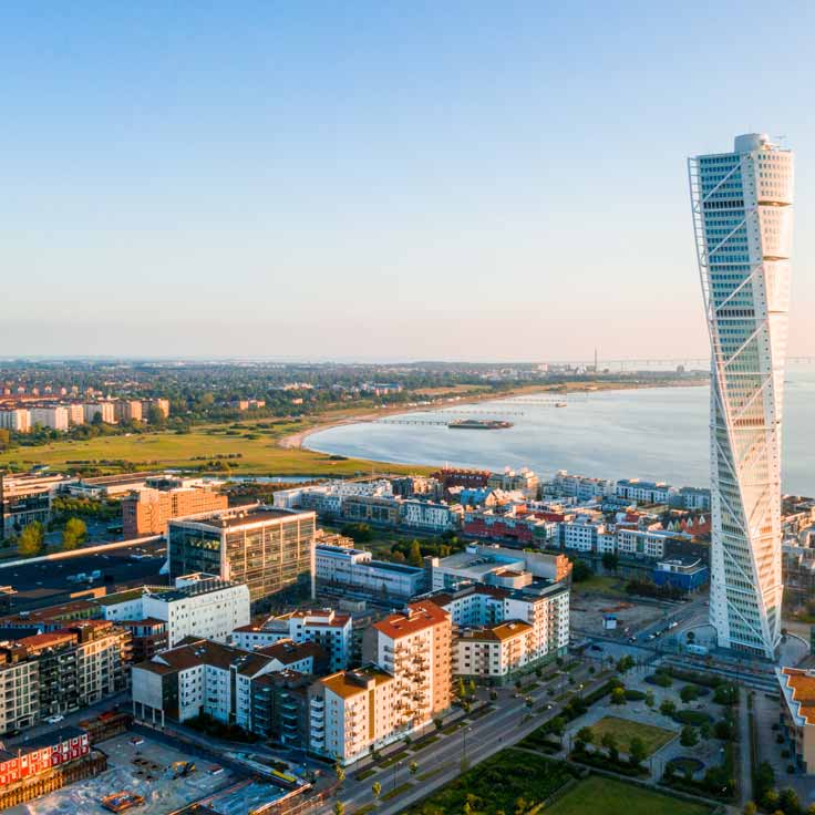 Aerial view of Malmö city featuring the iconic Turning Torso and the coastline in the background.