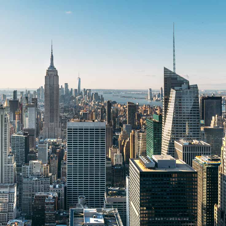 Aerial view of New York City skyline featuring the Empire State Building and One World Trade Center under a clear blue sky.