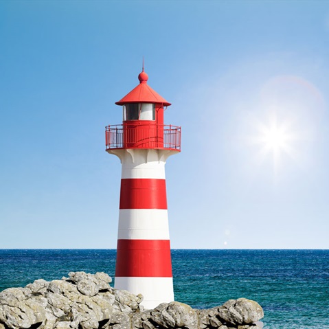 Ein rot-weiß gestreifter Leuchtturm steht auf Felsen am Meer unter einem klaren Himmel.