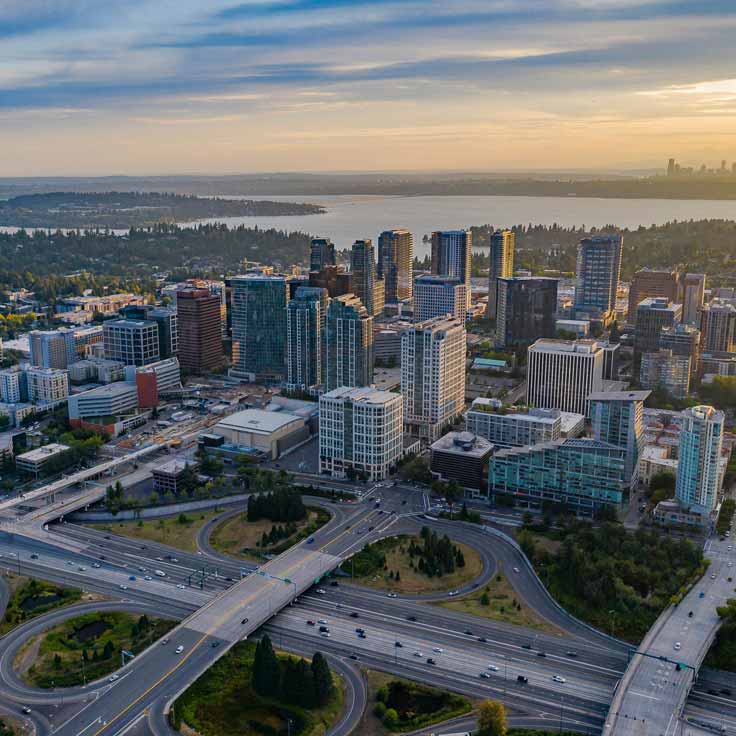 Aerial view of a modern cityscape with tall buildings, highways, and a lake in the background at sunset.