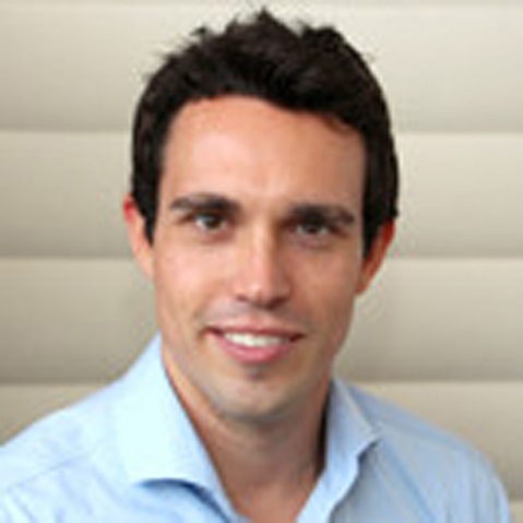 Ein Mann trägt ein blaues Hemd und steht vor einer hellen, strukturierten Wand.