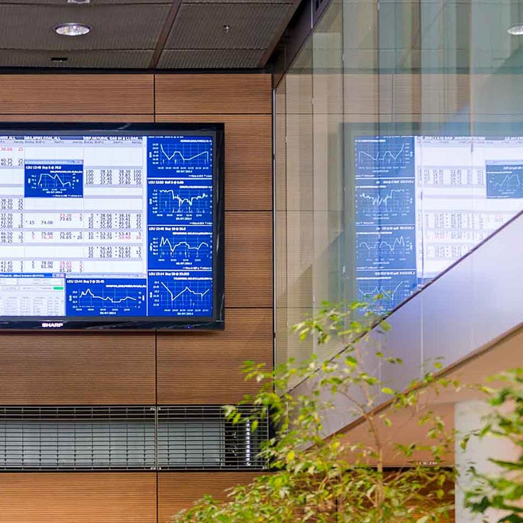 Ein Bildschirm zeigt Finanzdaten und Diagramme in einem modernen Bürogebäude, umgeben von einer Pflanzenanlage.