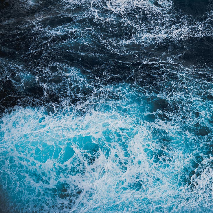 Eine Ansicht des Ozeans mit tiefblauen und türkisfarbenen Wellen, die sich an der Oberfläche brechen.