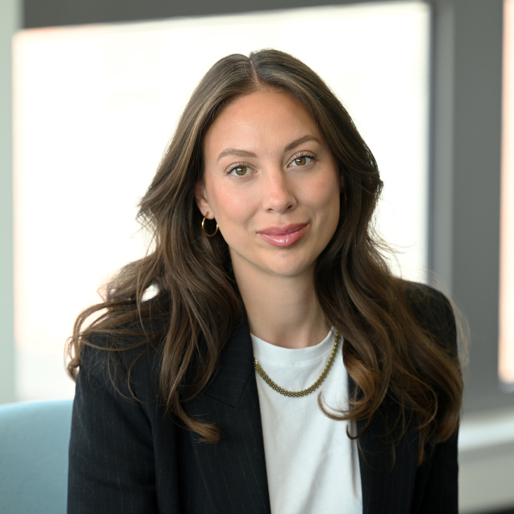 A woman with long, wavy hair wears a black blazer and a necklace. The background is bright and modern.