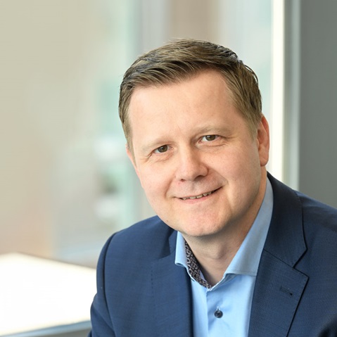 A man in a blue suit sits in a modern office with large windows. He is wearing a light blue shirt with an elegant pattern. Portrait von Martin Modzelewski.