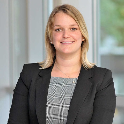 A person in a black suit with blonde hair stands against a light background. Portrait of Anna-Lena Meyer.