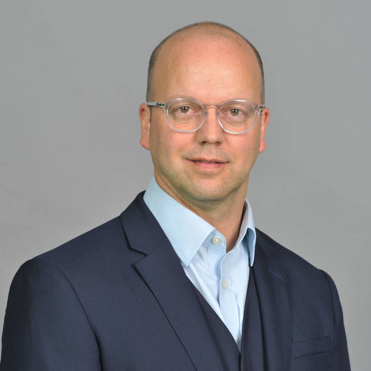 A man is wearing a suit and a collared shirt. The background is grey and neutral. Portrait of Maarten Abele.