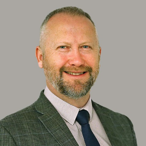 A man in a checked suit and striped shirt poses against a grey background. Portrait of Mark Fleming.