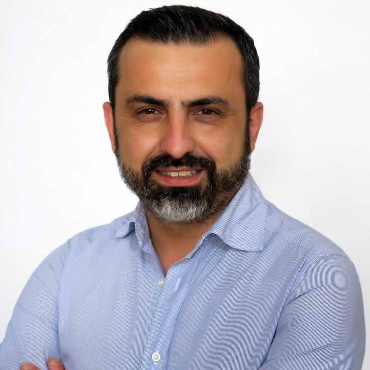 A man with crossed arms is wearing a light blue shirt against a white background. Portrait of Nello D’Orazi.
