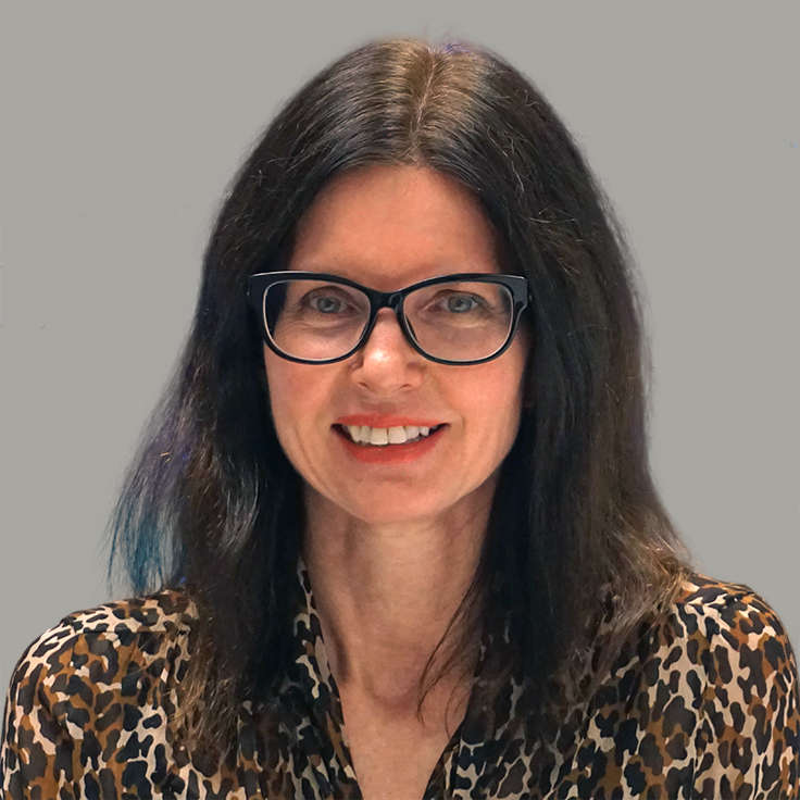 A person with long dark hair is wearing a leopard-print shirt. The background is grey. Portrait of Sue Vincent.