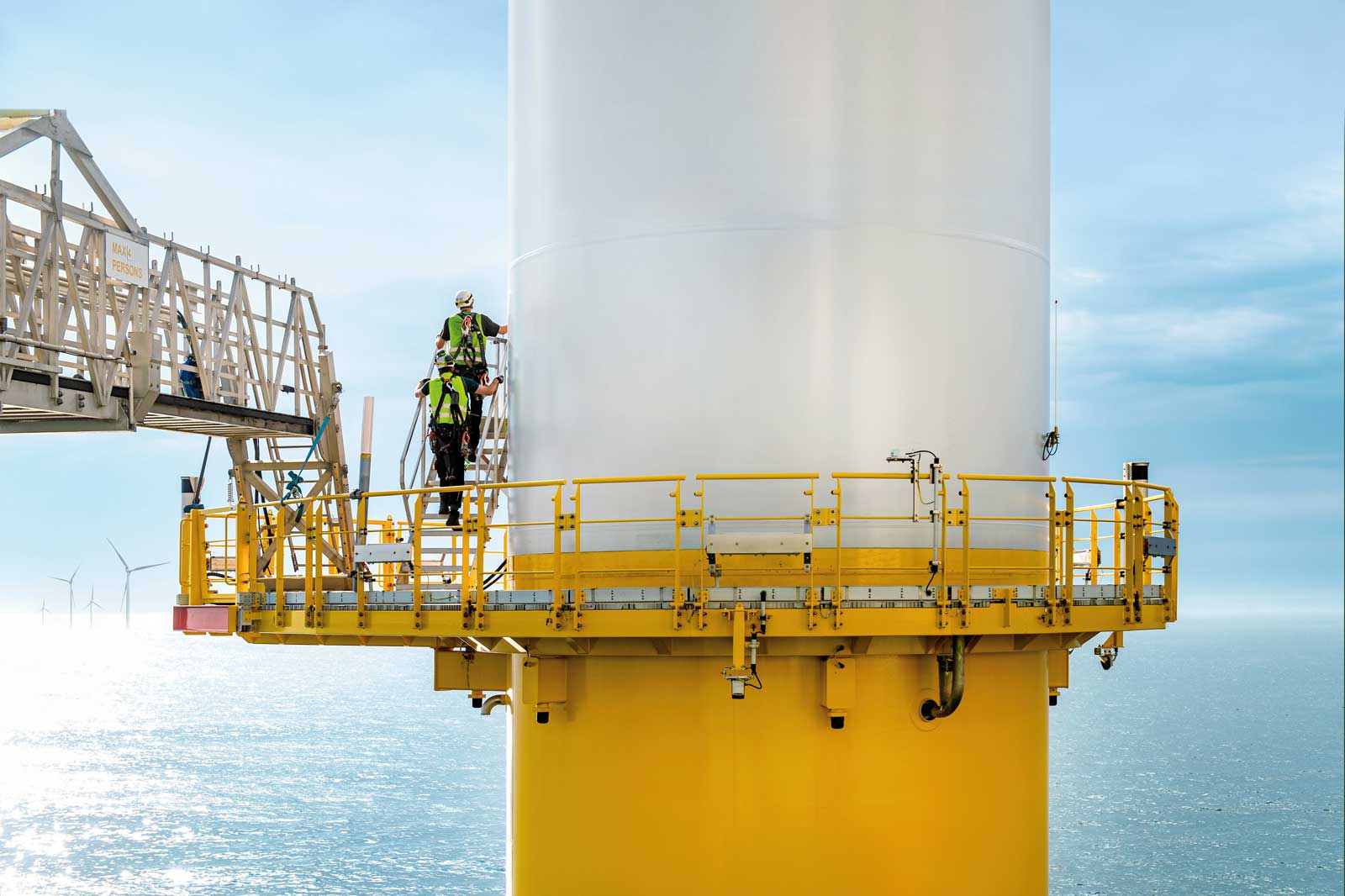 Ein Arbeiter, der an einem gelben Offshore-Windkraftwerk auf dem Meer arbeitet, umgeben von ruhigem Wasser und Himmel.