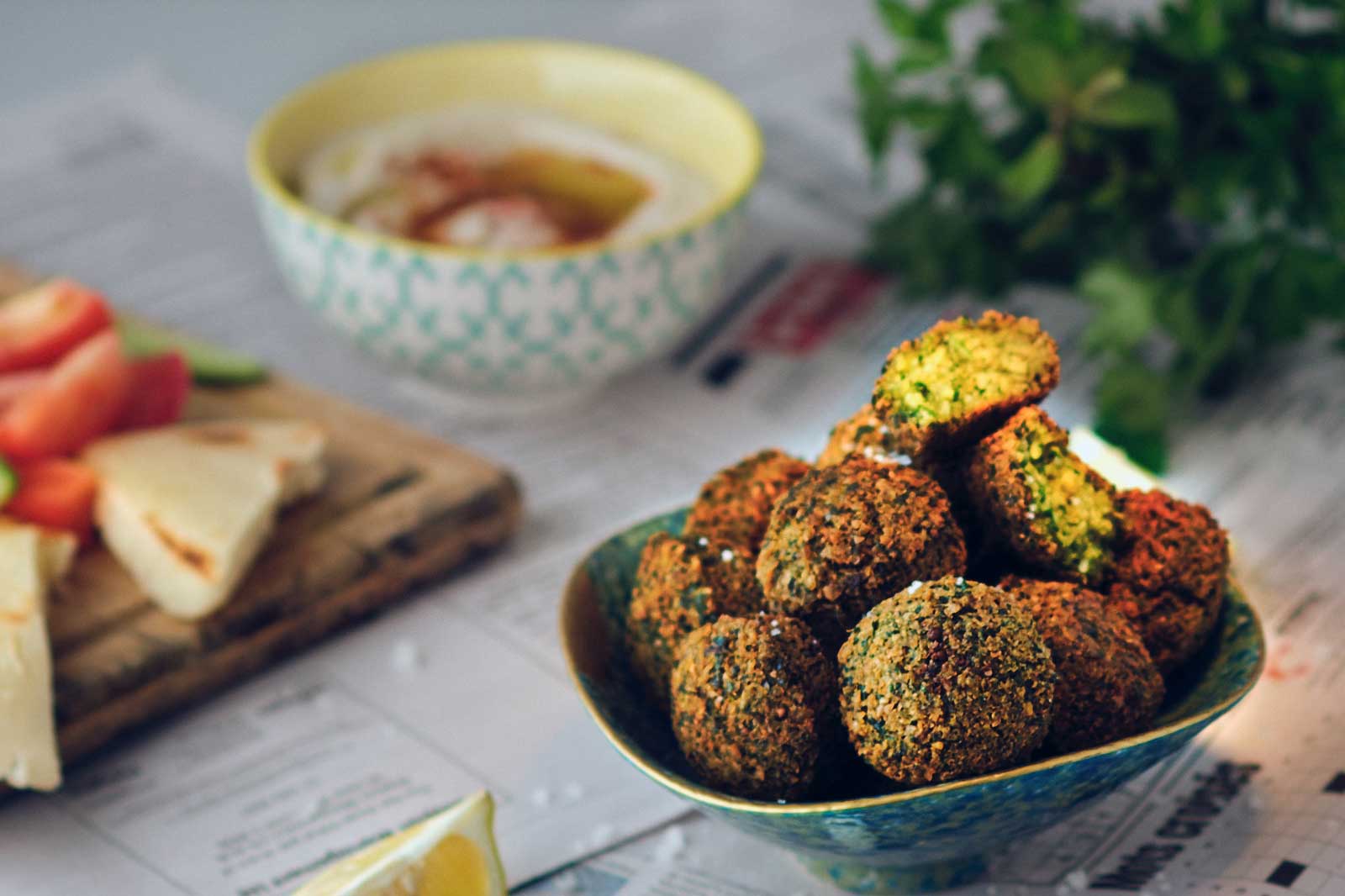 Eine Schüssel mit knusprigen Falafelbällchen, serviert mit frischen Tomaten, Fladenbrot und einer Schüssel Sauce.