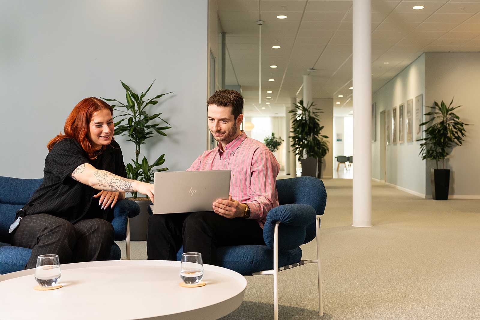 Ein Mann und eine Frau sitzen in einem modernen Büro und schauen gemeinsam auf einen Laptop.