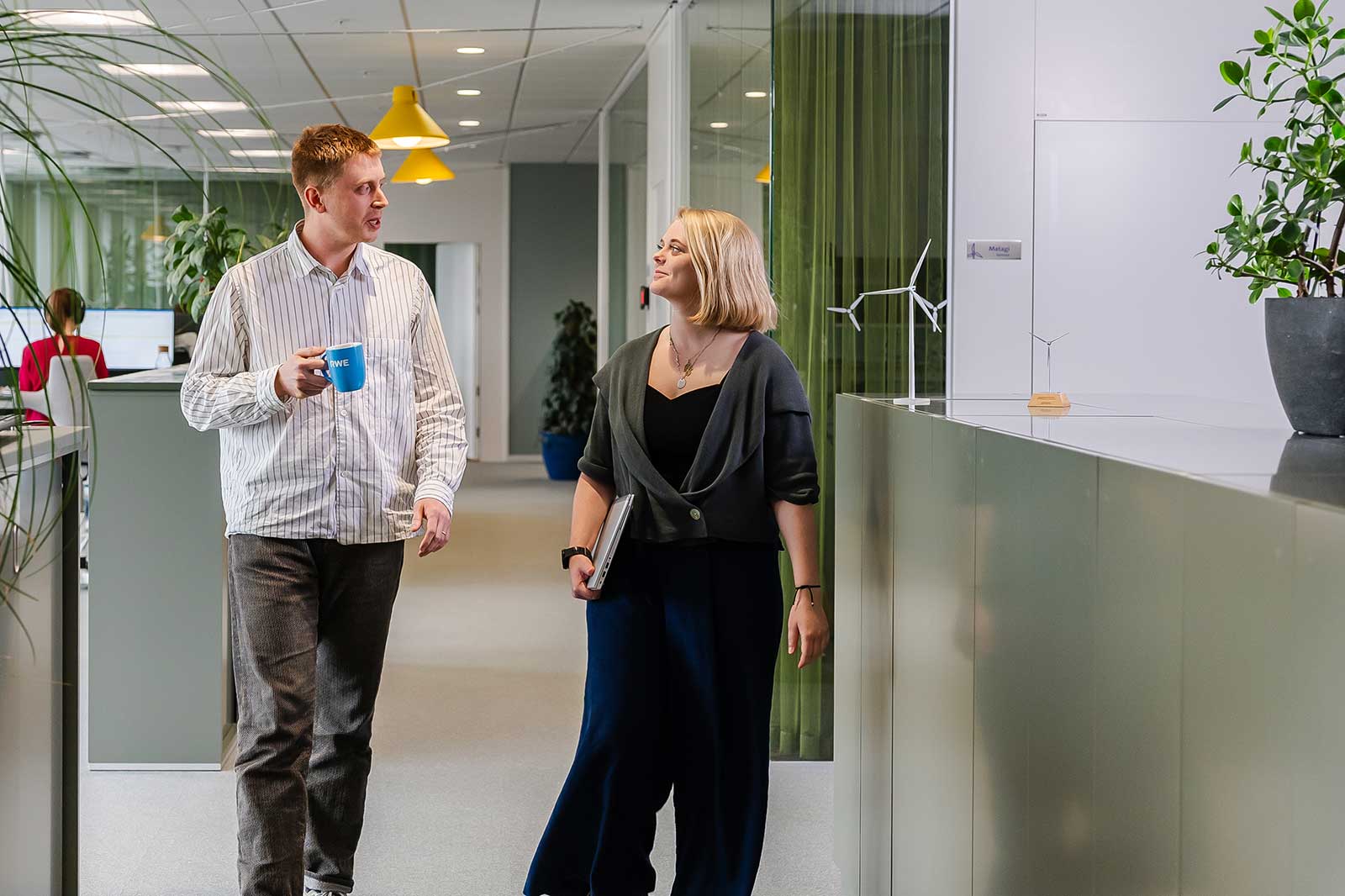 Zwei Kollegen gehen und sprechen in einem modernen Büro mit Pflanzen und dekorativen Gegenständen.
