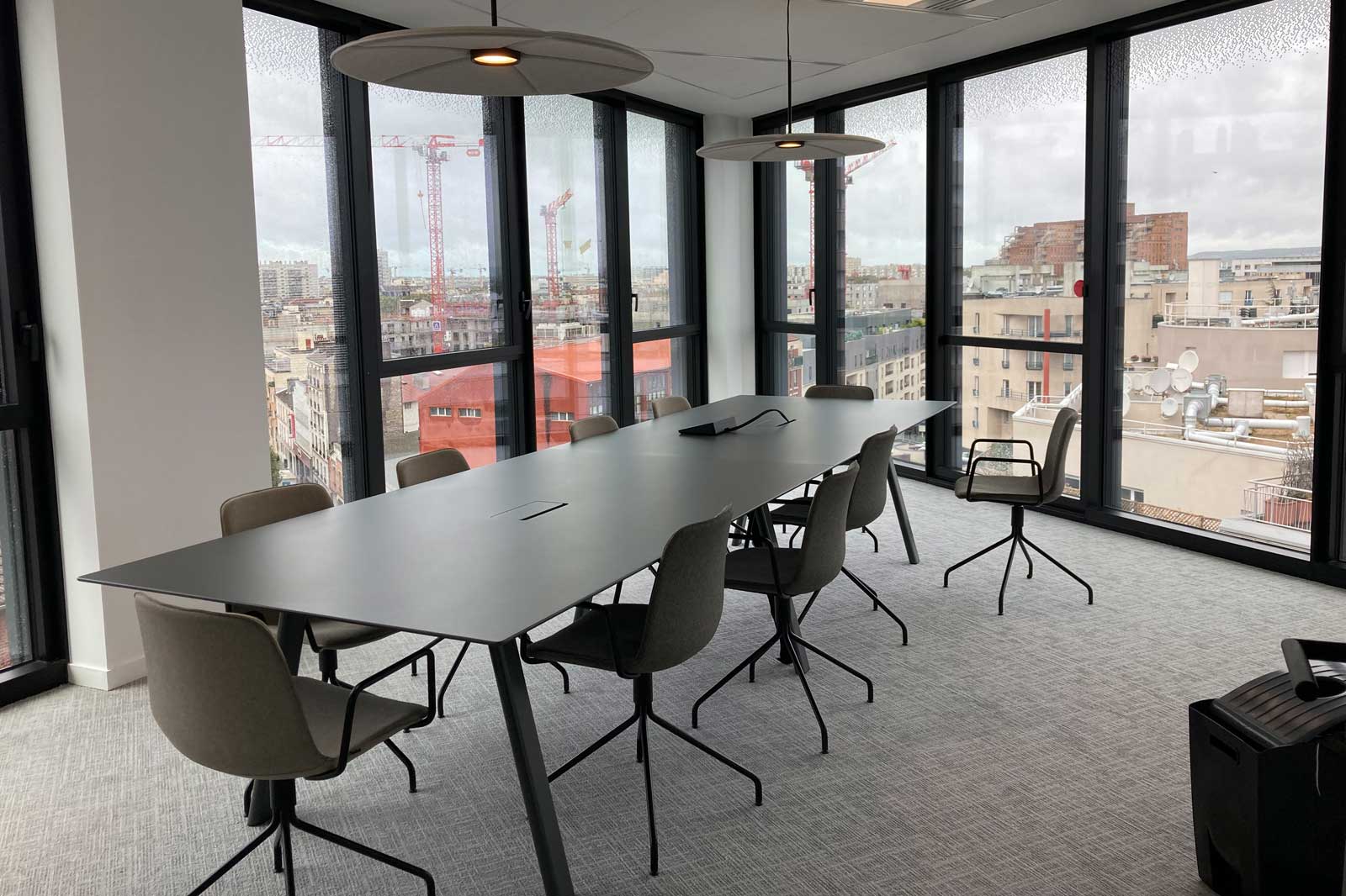 Ein modernes Besprechungszimmer mit einem langen Tisch, Stühlen und großen Fenstern mit Blick auf die Stadtlandschaft.