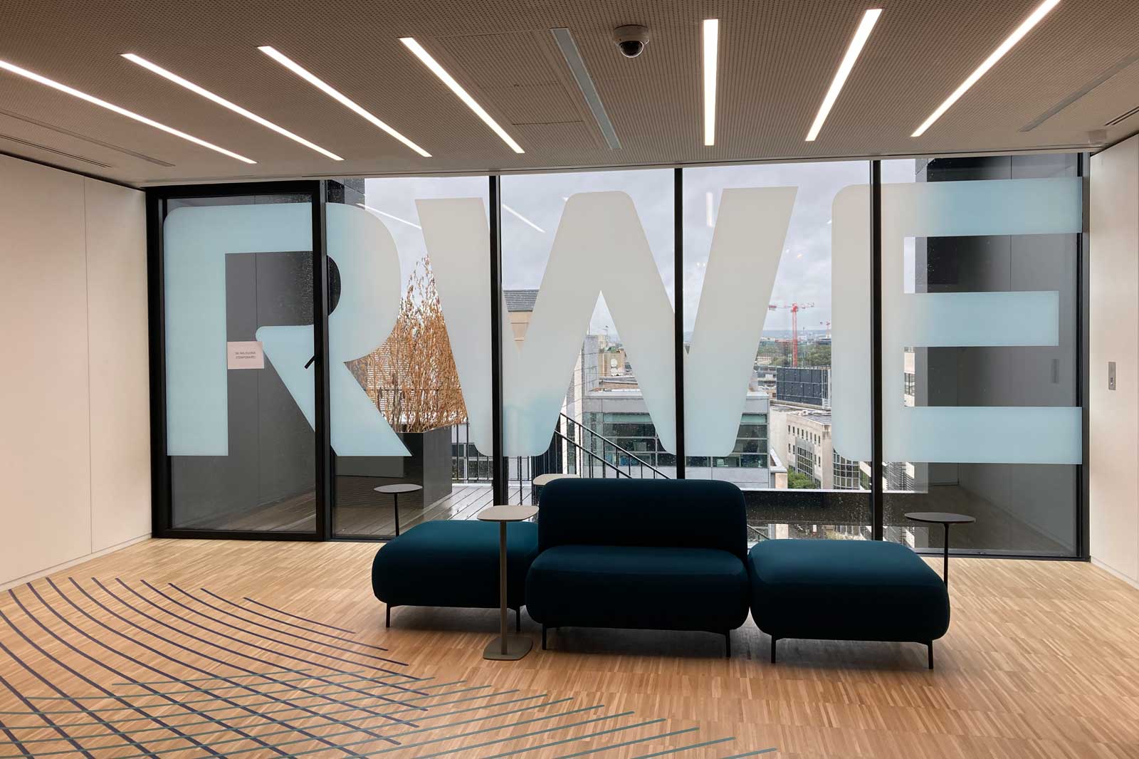 Moderne Büroräume mit einem blauen Sofa und einer großen Fensterfront, auf der die Buchstaben 'RWE' stehen.