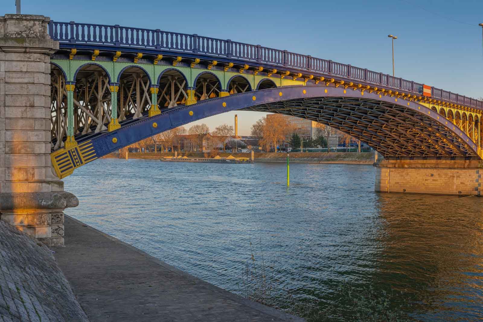 Eine farbenfrohe Brücke mit grünen, blauen und gelben Akzenten, die über einen ruhigen Fluss führt.