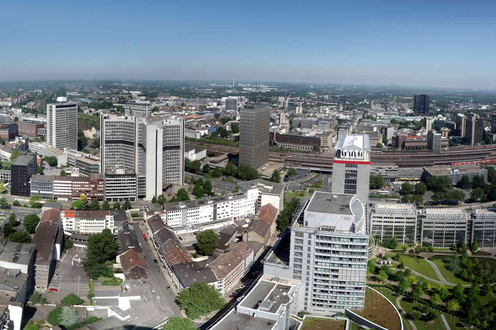 Luftaufnahme einer Stadtlandschaft mit modernen Gebäuden und einer grünen Parklandschaft im Vordergrund.