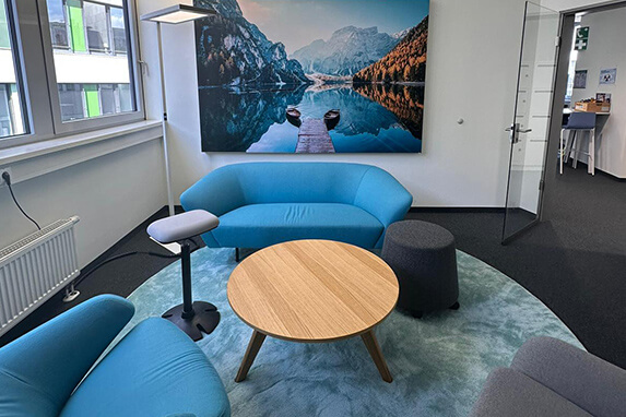 Ein moderner Büroraum mit blauen Sofas, einem runden Tisch und einem beeindruckenden Bergbild an der Wand.