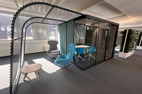 Ein modernes Büro mit einem Glaskonferenzraum, blauen Stühlen und einem gemütlichen Lesesessel im Vordergrund.